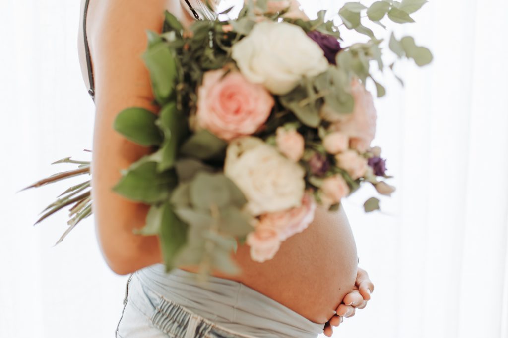 Ausschnitt eines Babybauches mit einem Blumenstrauß