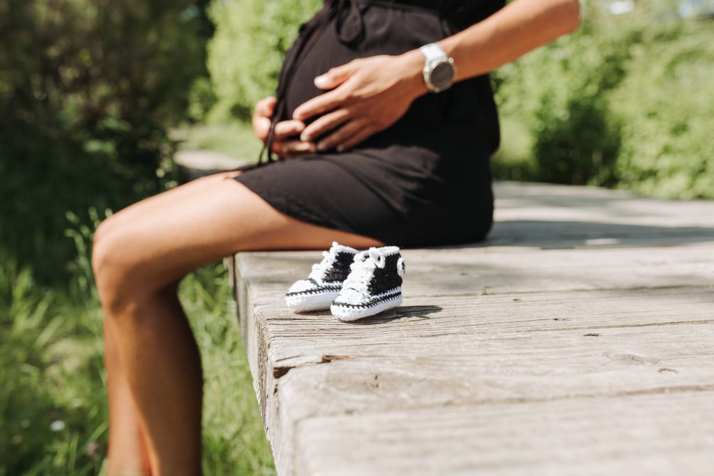 Ausschnitt eines Babybauches mit kleinen gehäkelten Babyschuhen