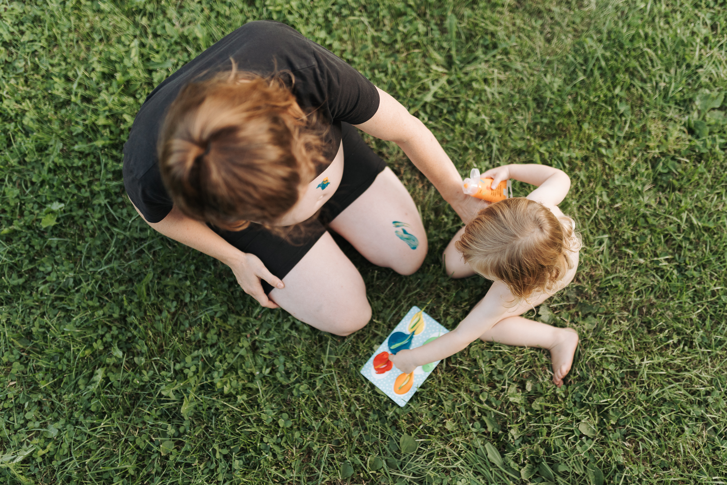 Schwangere Frau im Schwarzwald sitzt mit ihrer Tochter im Garten und bemalen den Babybauch mit Fingermalfarben.