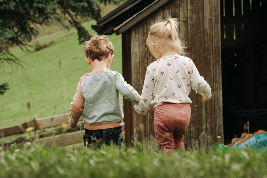 Ein kleines Mädchen und ein kleiner Junge laufen Händchen haltend im eigenen Garten.